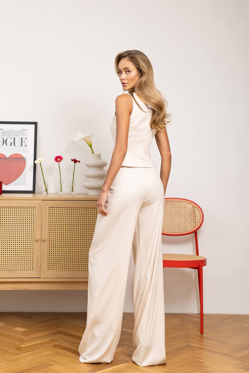 Woman in a white outfit standing in a room with a red chair and wooden cabinet.