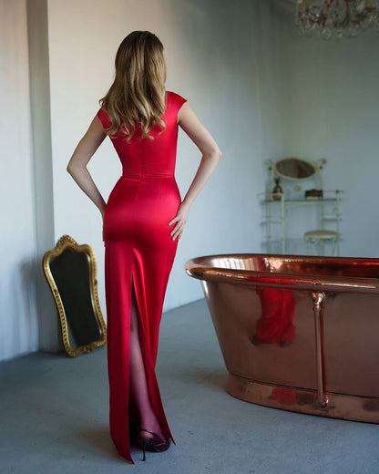 Woman in a red dress standing next to a copper bathtub in an elegant room.