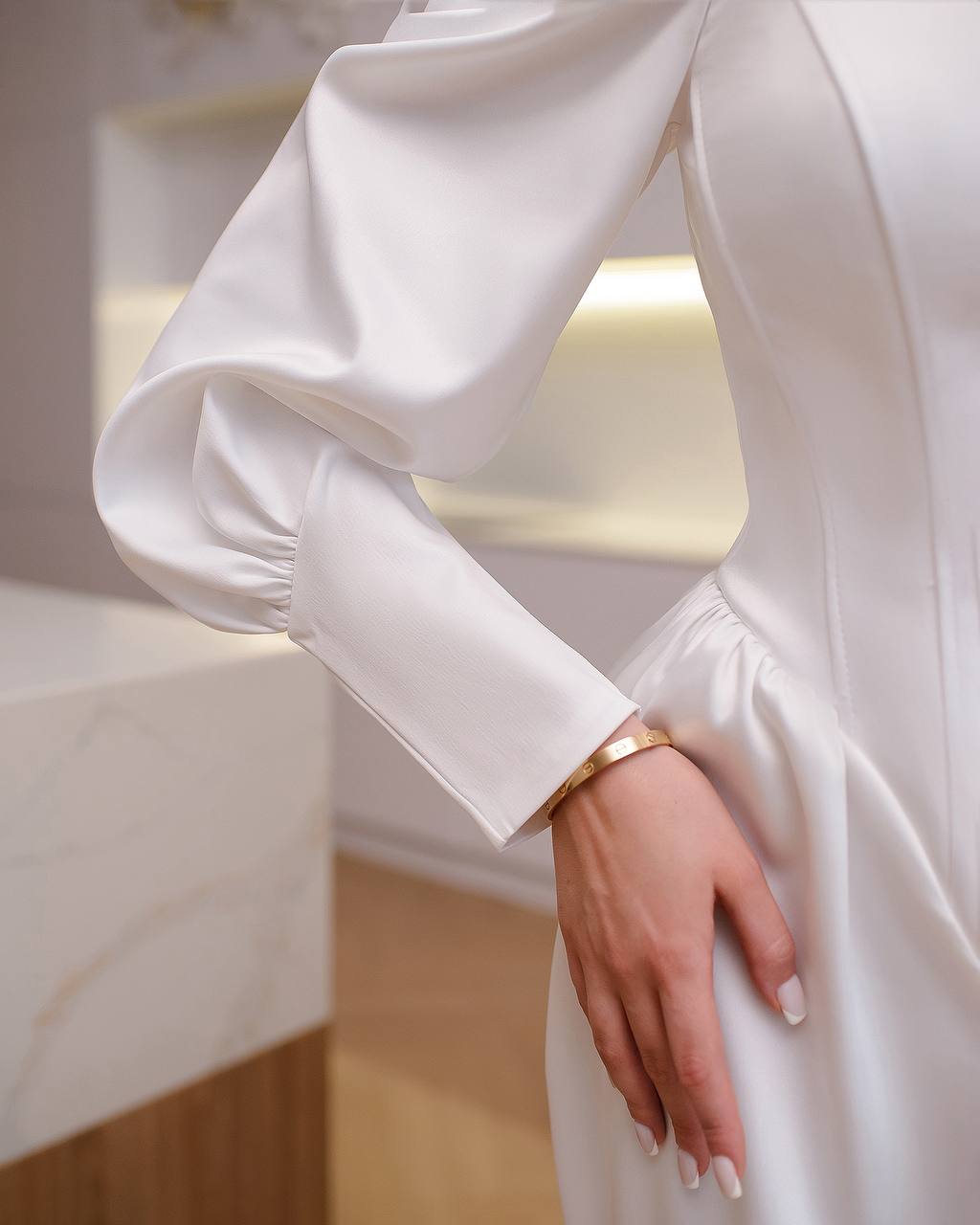 Close-up of a person wearing a white dress with long sleeves and a gold bracelet.