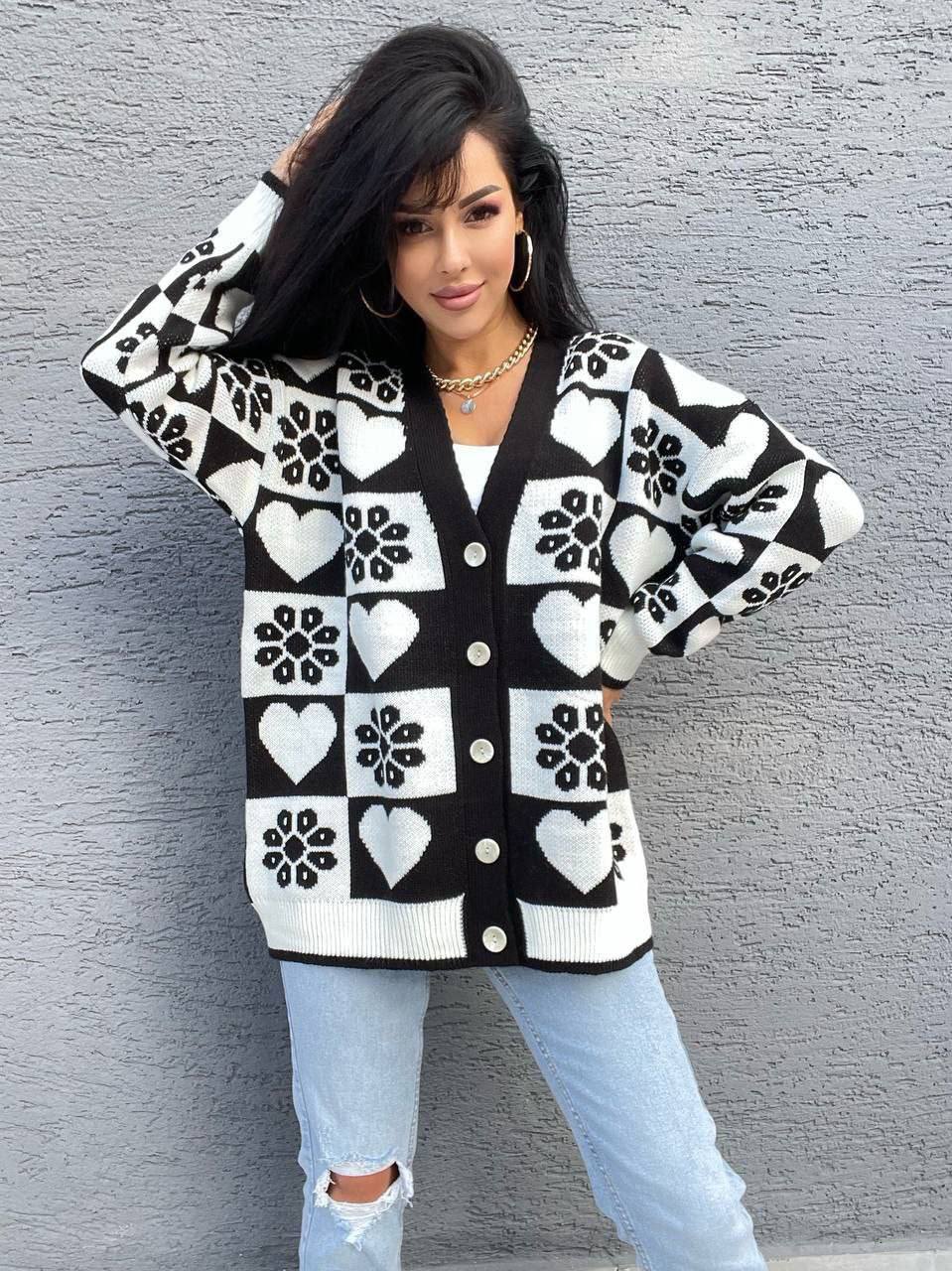Woman wearing a black and white patterned cardigan against a gray wall