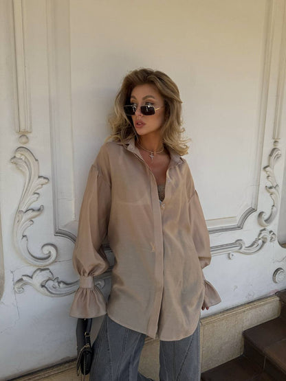 Woman wearing a beige shirt and sunglasses against an ornate wall.