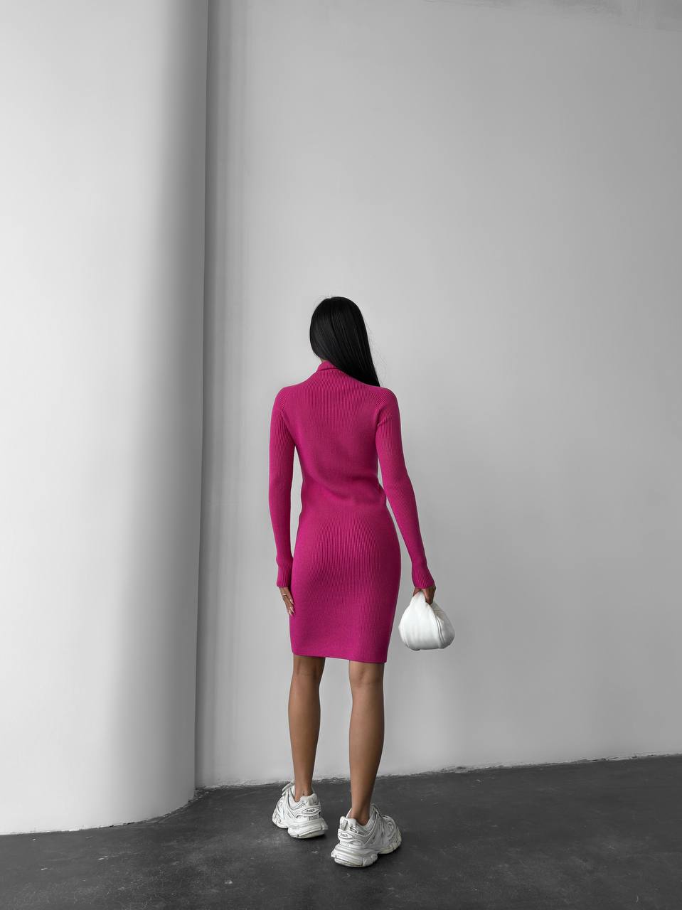 Person wearing a pink dress standing against a plain wall.