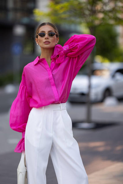 Woman wearing a bright pink shirt and white pants on a street.