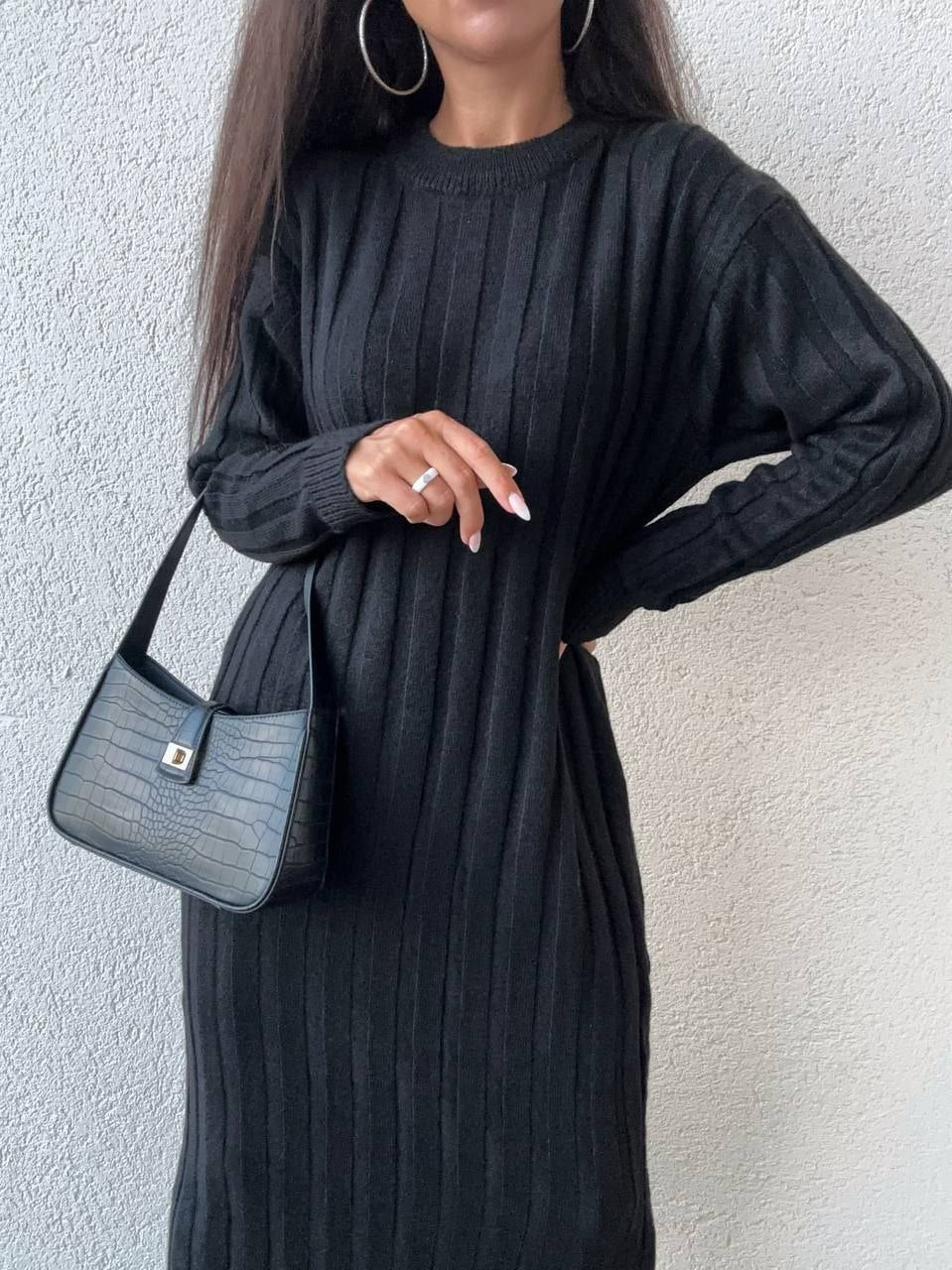 Woman wearing a black ribbed dress holding a blue handbag against a white background