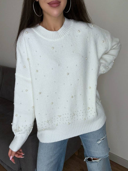Person wearing a white sweater with pearl embellishments and ripped jeans indoors.