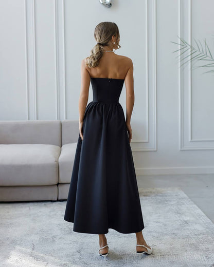 Woman wearing a black strapless dress in a room with white walls and a gray sofa.