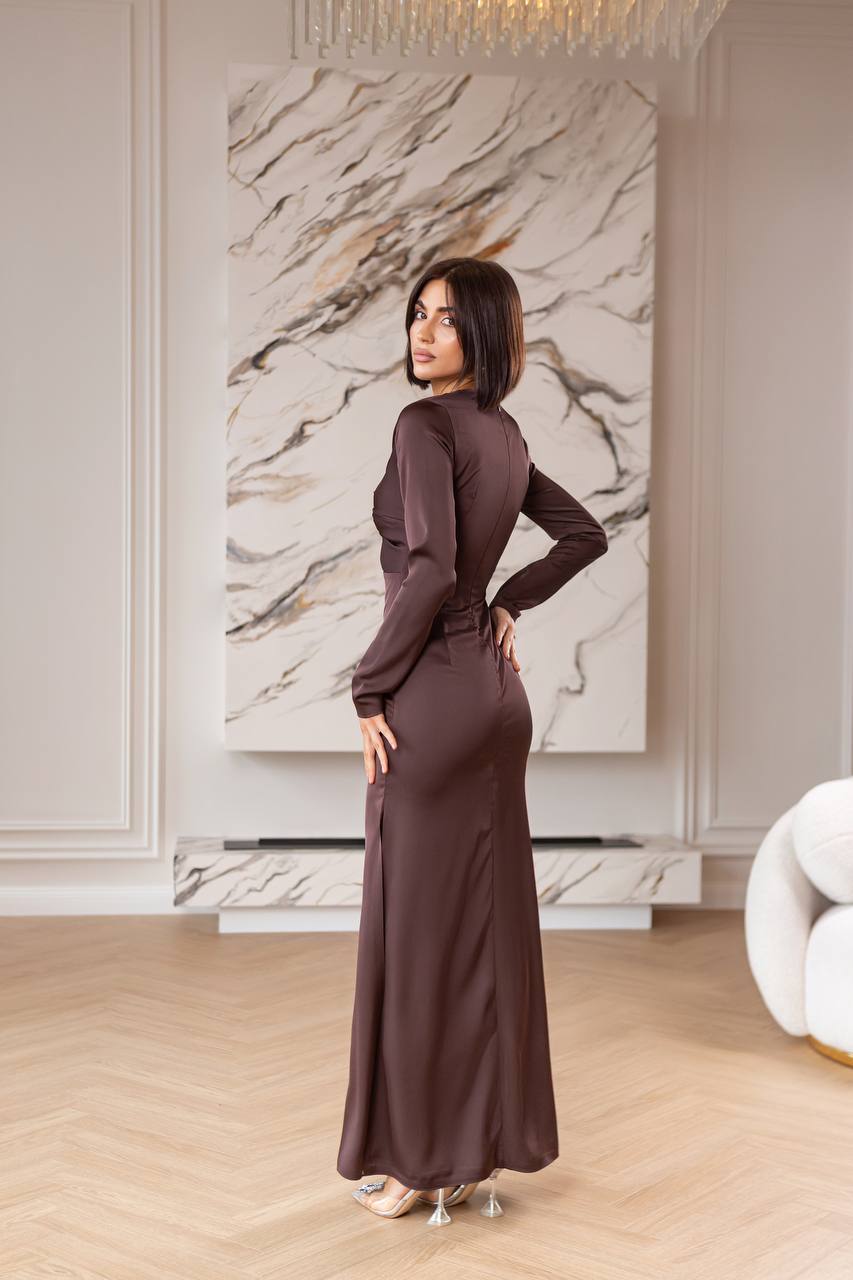 Woman in a long brown dress standing in a stylish room with marble wall.