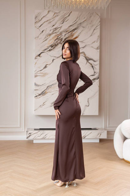 Woman in a long brown dress standing in a stylish room with marble wall.
