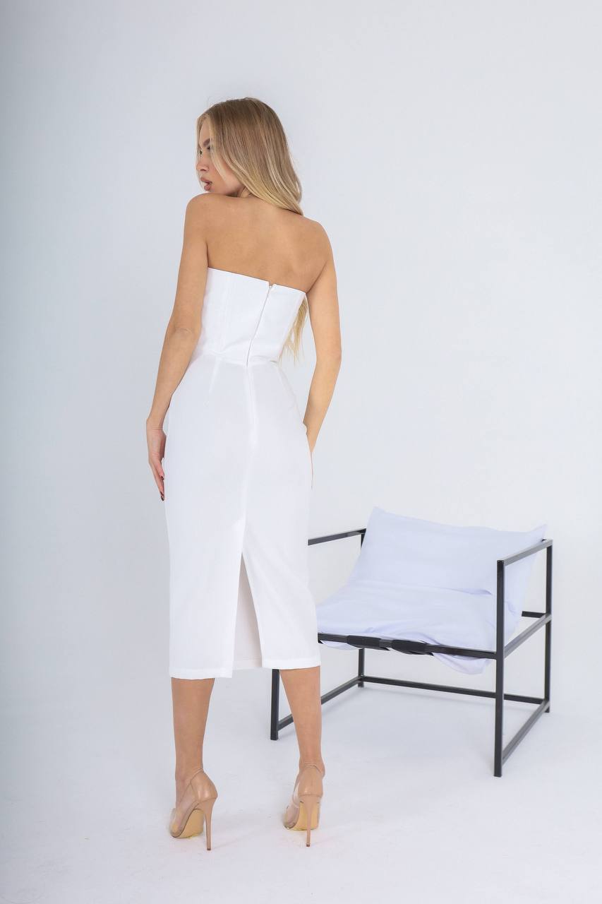 Woman wearing a white strapless dress standing in a minimalistic setting with a chair.