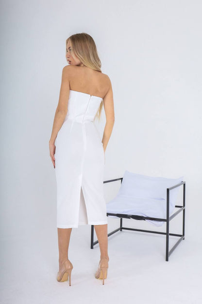 Woman wearing a white strapless dress standing in a minimalistic setting with a chair.