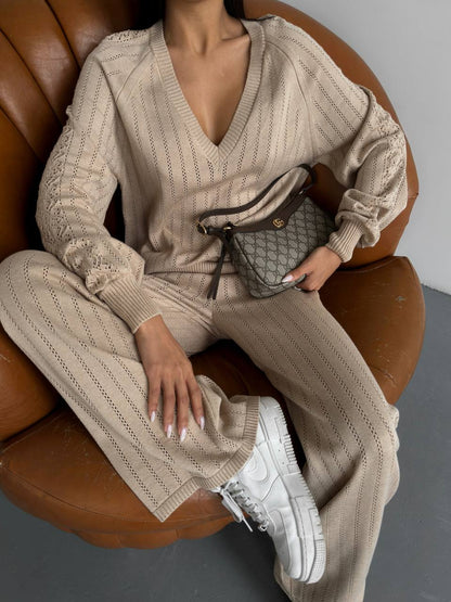 Person wearing a beige knit outfit sitting on a brown chair holding a handbag.