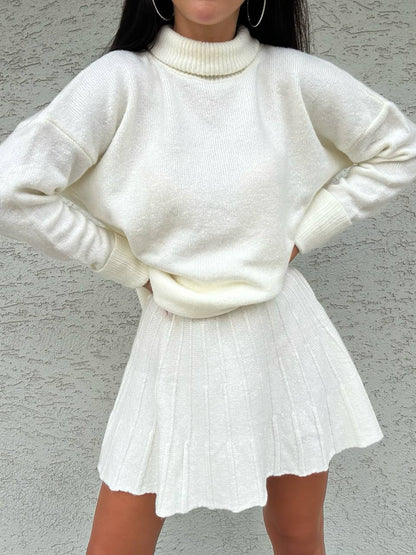 Person wearing a white sweater and skirt against a gray background