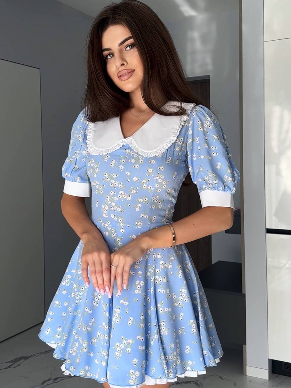 Woman wearing a blue floral dress with a white collar in an indoor setting