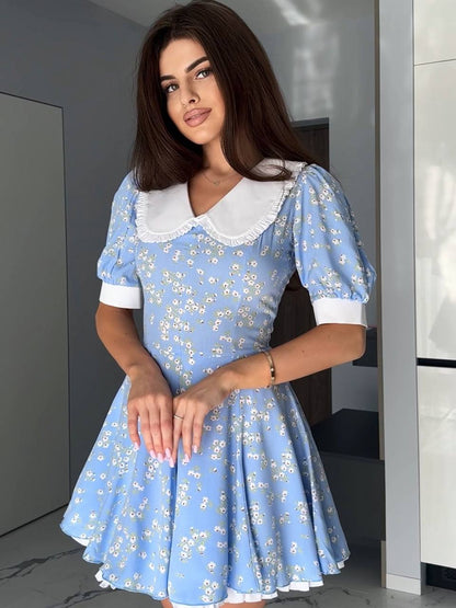 Woman wearing a blue floral dress with a white collar in an indoor setting