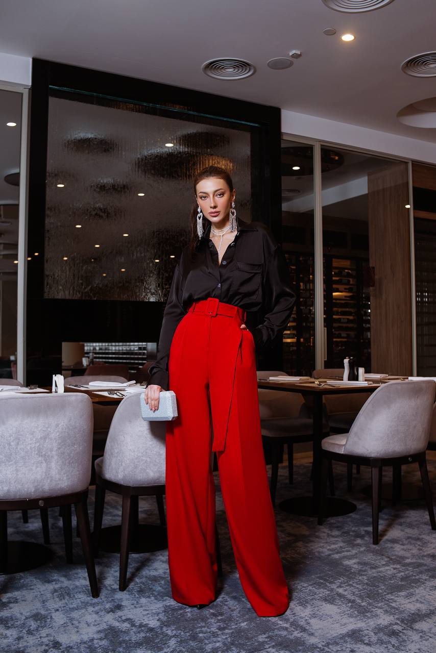 Woman in a black top and red pants standing in a modern restaurant.