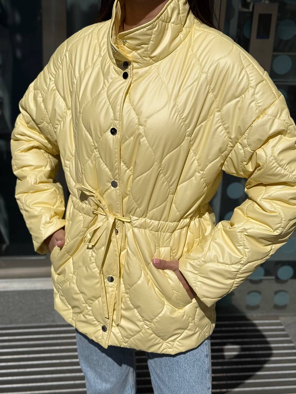 Person wearing a light yellow quilted jacket with a dark background