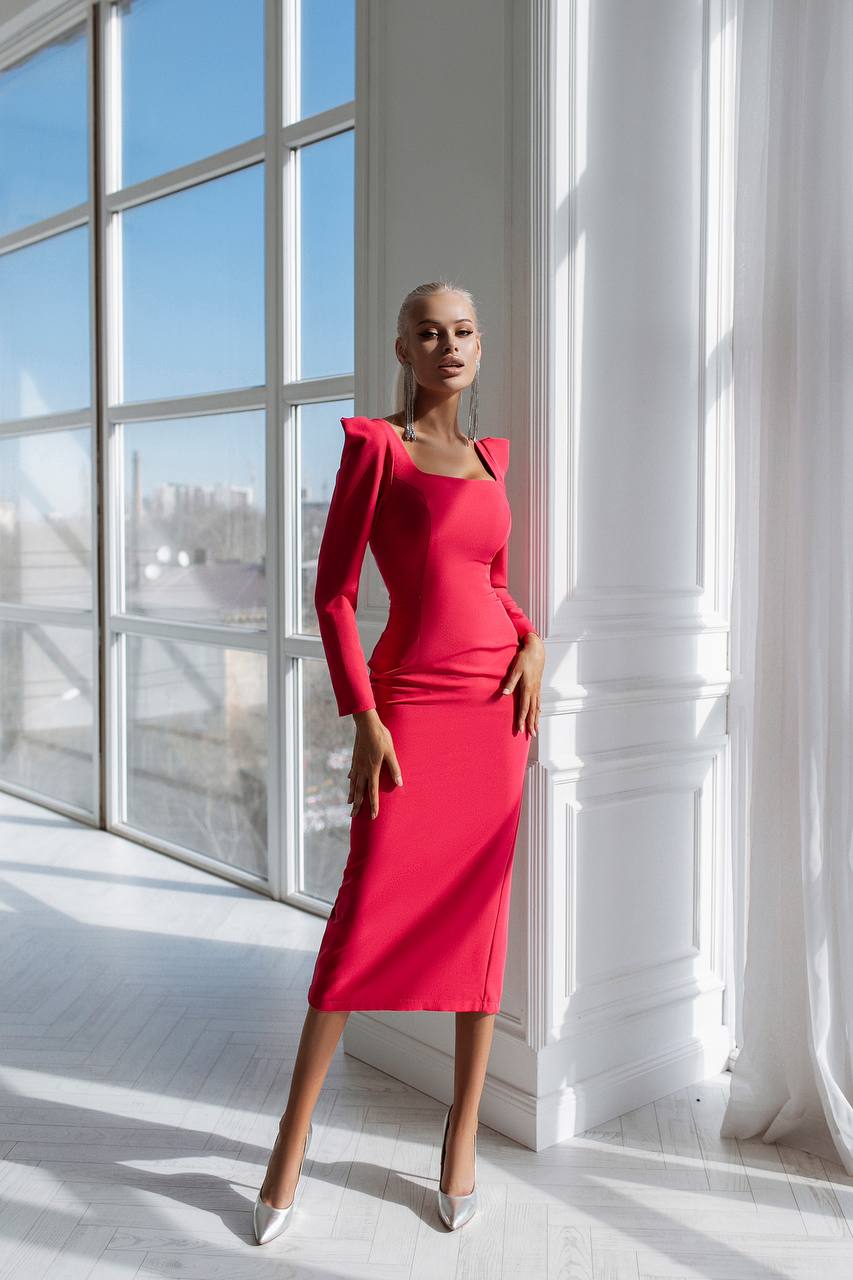 Woman in a red dress standing in a bright room with large windows.
