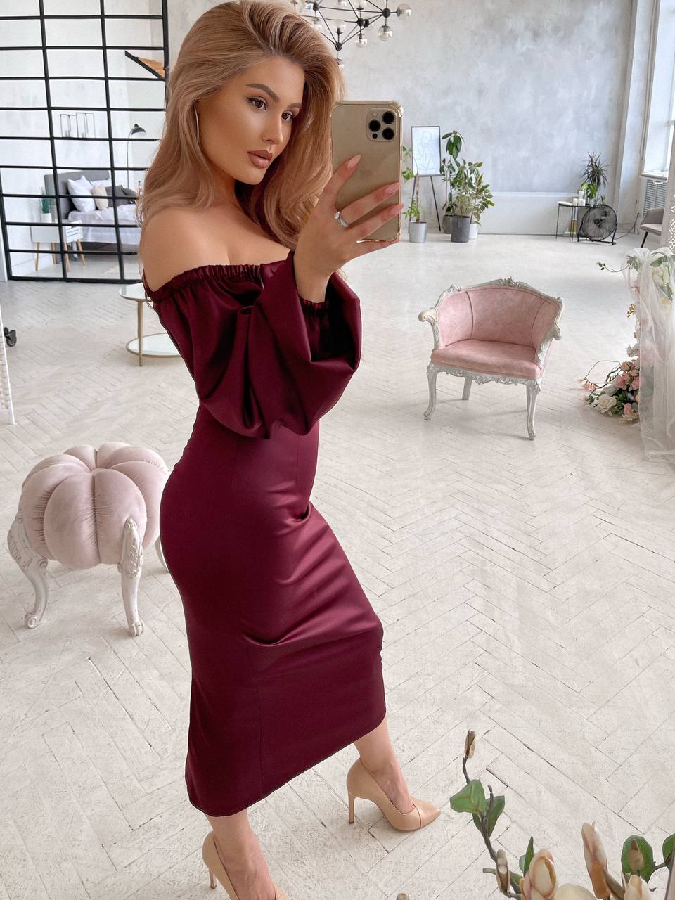 Woman in a burgundy off-shoulder dress taking a mirror selfie in a stylish room.