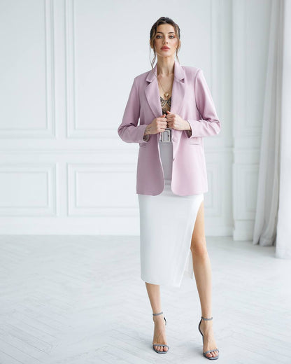 Woman wearing a pink blazer over a white dress in a minimalistic setting