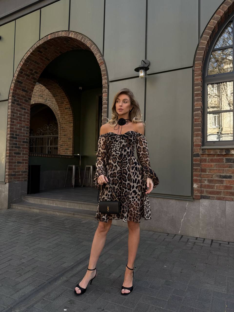 Woman in a leopard print dress standing in front of a building with arched doorways.