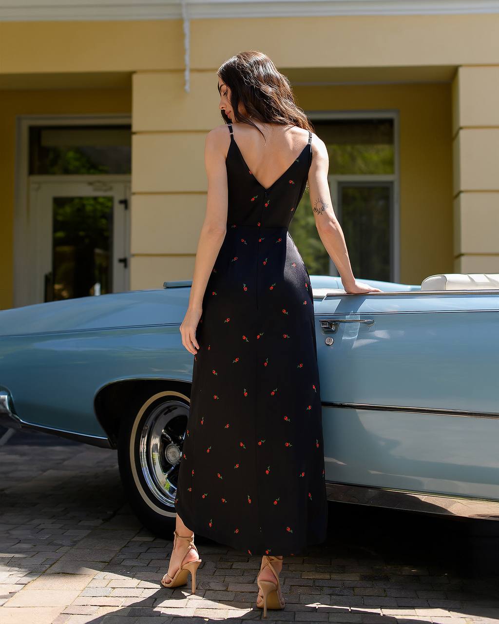 Woman in a black dress standing next to a vintage blue car