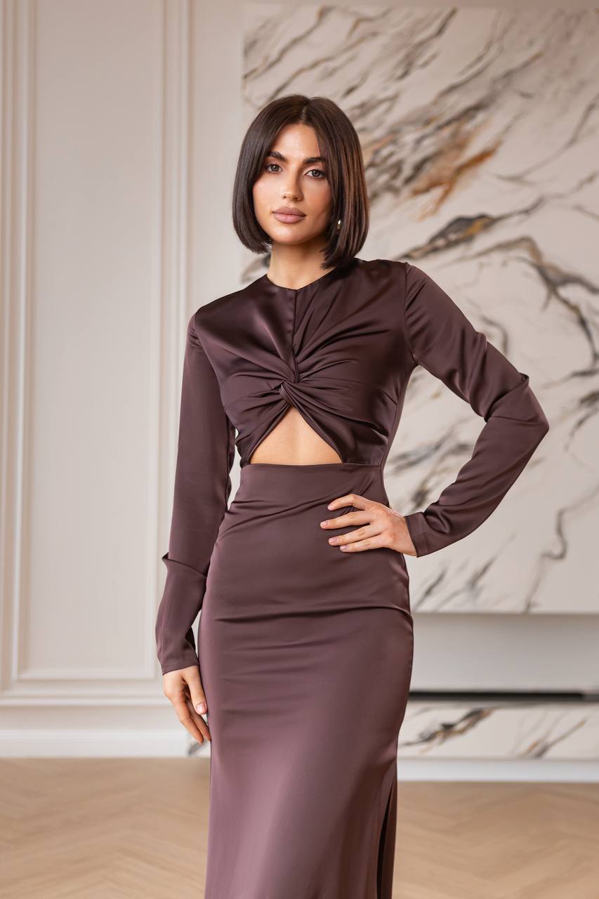 Woman wearing a brown dress with cut-out design in a room with marble wall.