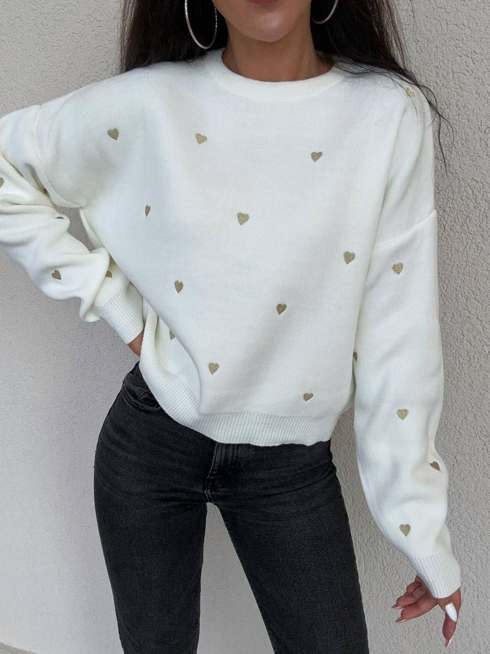 White sweater with heart patterns worn by a person against a neutral background