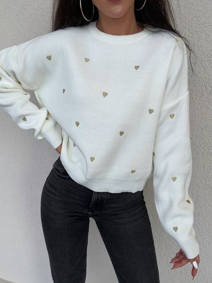 White sweater with heart patterns worn by a person against a neutral background
