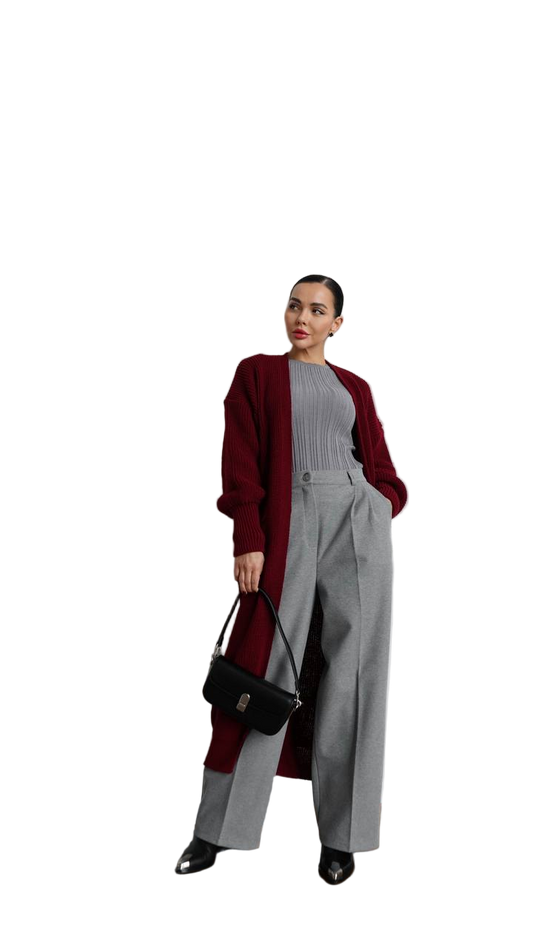 Woman wearing a burgundy cardigan, gray sweater, and wide-leg pants holding a black handbag on a white background