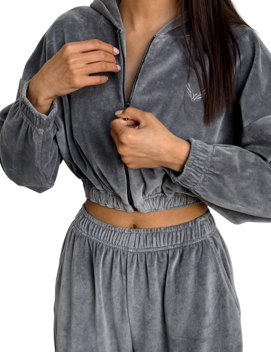 Person wearing a gray velour tracksuit with a brand logo on a white background