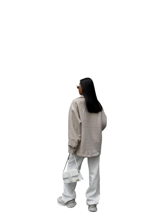 Person wearing a beige sweater and white pants with a white bag on a white background