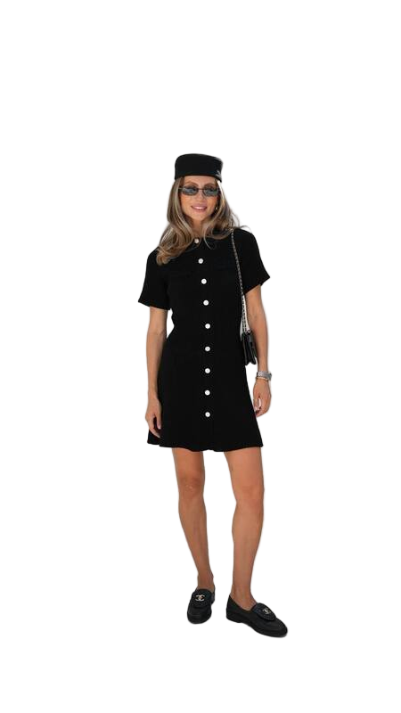 Person wearing a black dress with buttons and a matching hat on a white background