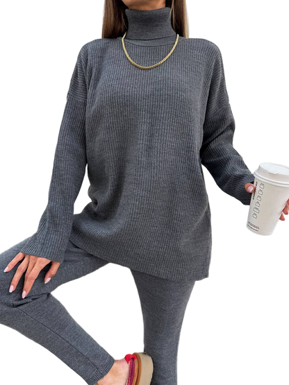 Person wearing a gray ribbed sweater and pants holding a coffee cup on a white background