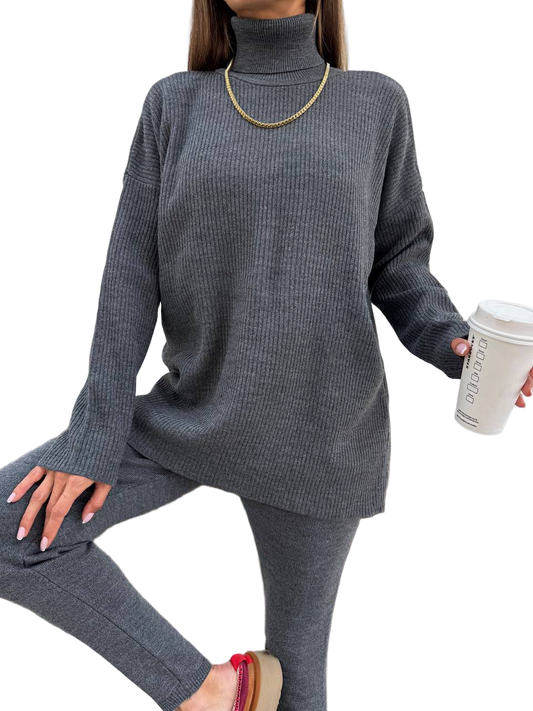 Person wearing a gray ribbed sweater and pants holding a coffee cup on a white background
