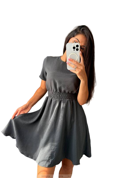 Woman wearing a gray dress taking a mirror selfie on a white background