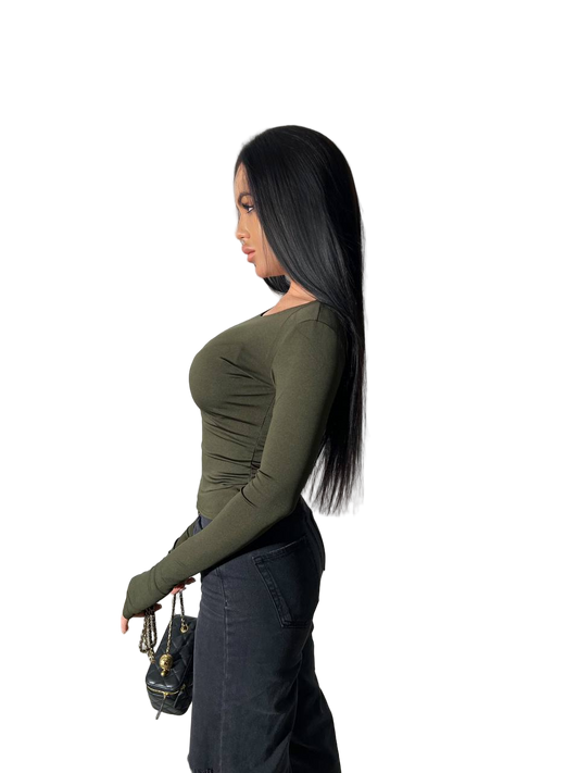 Woman wearing a green long-sleeve top and dark pants on a white background