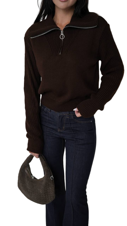 Person wearing a brown sweater and dark jeans holding a brown handbag on a white background