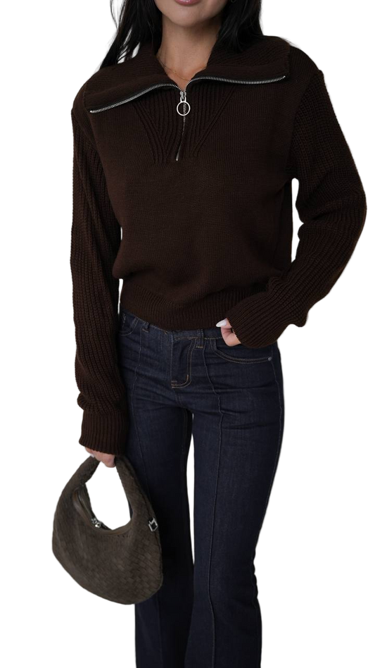 Person wearing a brown sweater and dark jeans holding a brown handbag on a white background