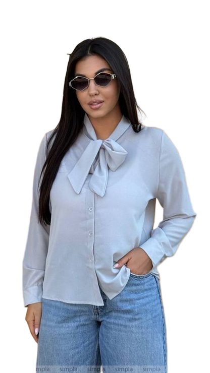Woman wearing a light blue blouse with a bow tie and jeans on a white background