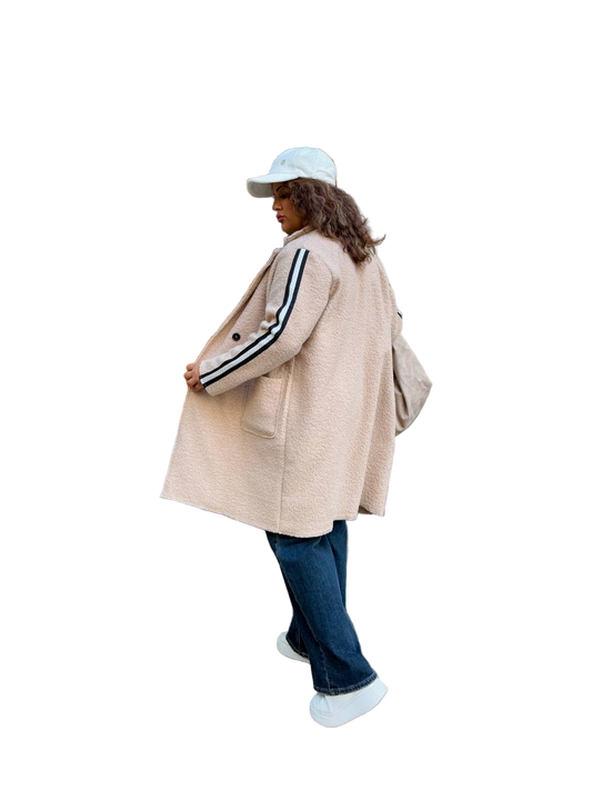 Person wearing a beige coat with black and white stripes, blue jeans, and a cap on a white background