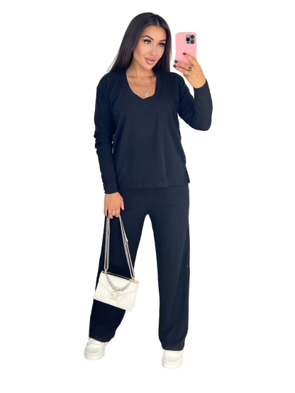 Woman taking a selfie wearing a dark blue outfit with a white handbag on a white background
