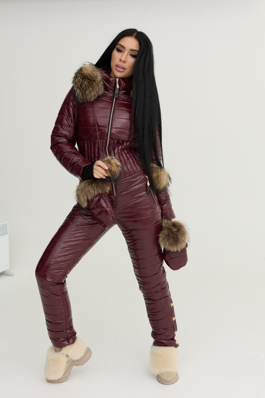 Woman wearing a maroon puffer jumpsuit with fur accents on a white background