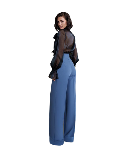 Woman wearing a black sheer top and blue pants on a white background