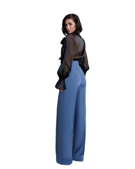 Woman wearing a black sheer top and blue pants on a white background