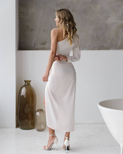 Woman in a white one-shoulder dress standing in a minimalistic room with decorative vases.