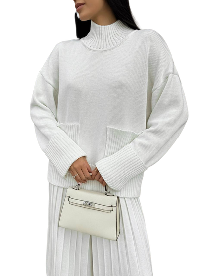 Person wearing a white ribbed sweater and holding a matching handbag on a white background