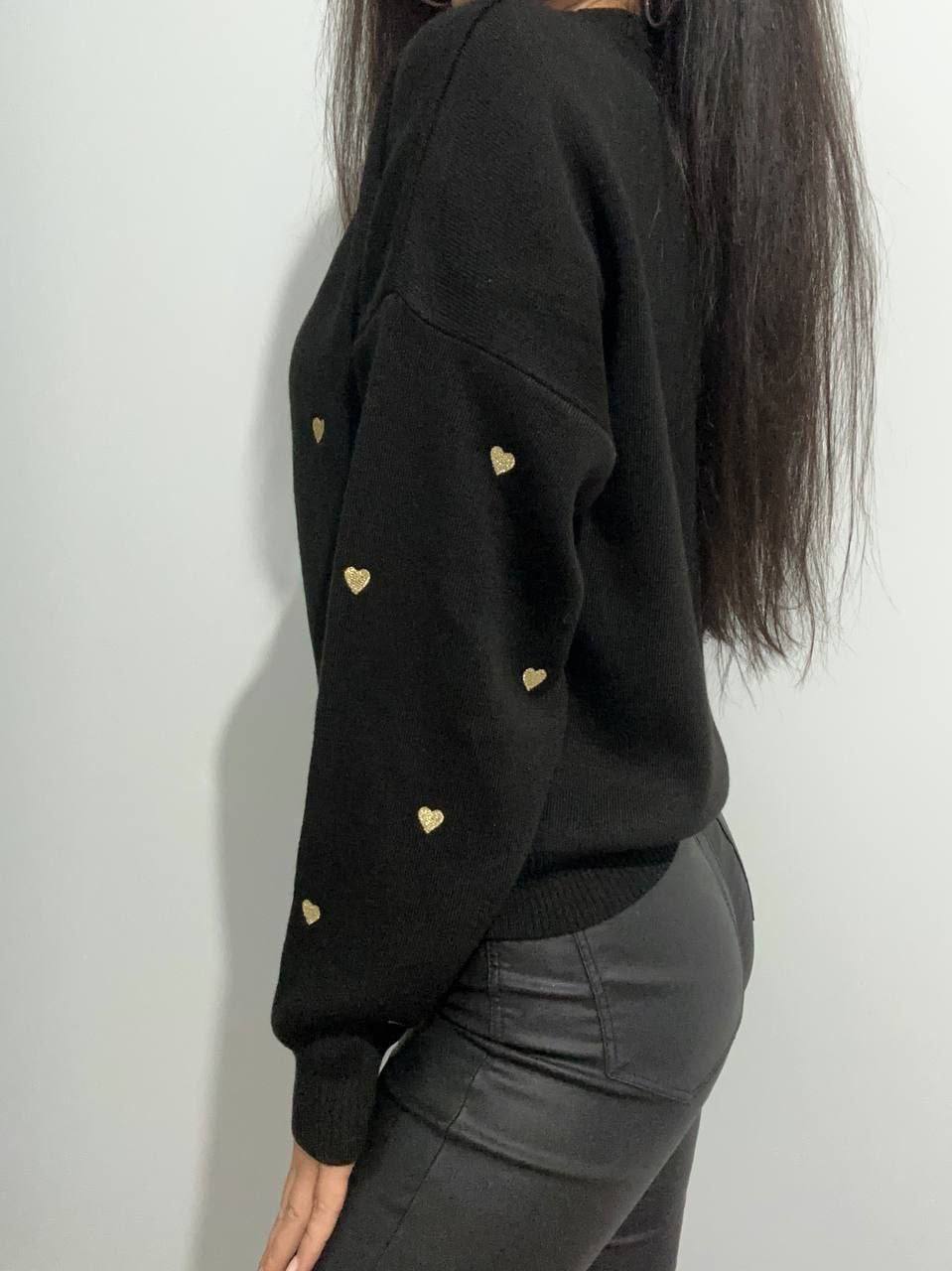 Black sweater with gold heart patterns worn by a person against a white background