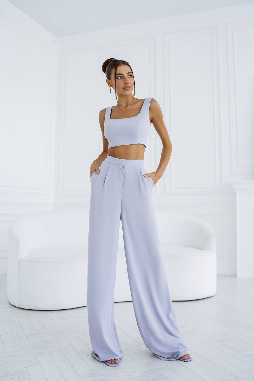 Woman wearing a white crop top and light gray wide-leg pants in a minimalistic setting.