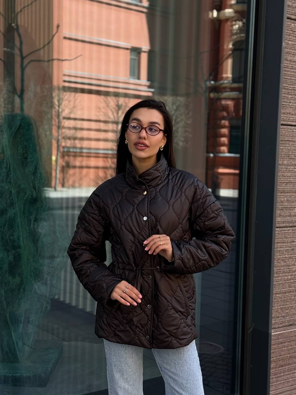 Woman wearing a dark brown puffer jacket standing in front of a reflective surface.