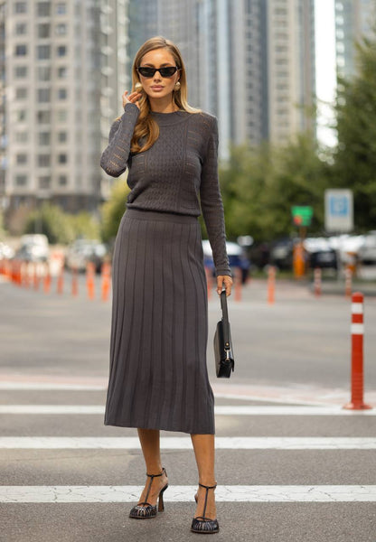 Woman in a gray outfit crossing a street with urban buildings in the background